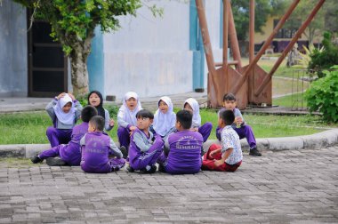 Riau-Endonezya, 28 Ağustos 2025: Mor ve beyaz üniformalı bir grup ilkokul öğrencisi açık havada asfalt zeminde oturuyorlar.