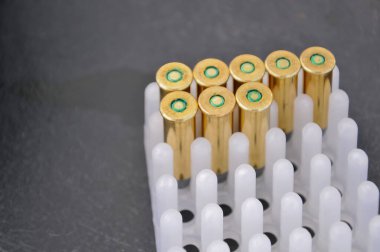 Birkaç parlak, boş mermi kovanı detaylı bir şekilde yakın plan çekimde gösteriliyor. Beyaz plastik bir tepside dikiliyorlar.. 