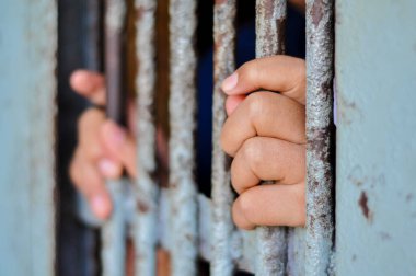 Mahkûmun elleri siyah arka planda parmaklıklar ardında.