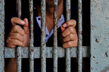 Mahkûmun elleri siyah arka planda parmaklıklar ardında.