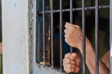 Mahkûmun elleri siyah arka planda parmaklıklar ardında.