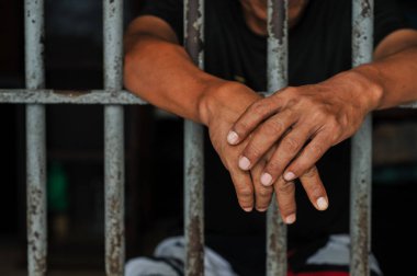 Mahkûmun elleri siyah arka planda parmaklıklar ardında.