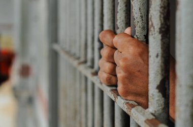 Mahkûmun elleri siyah arka planda parmaklıklar ardında.