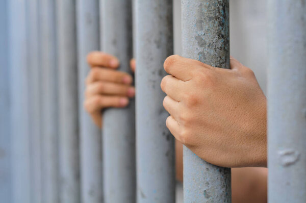 prisoner's hands behind bars with black background