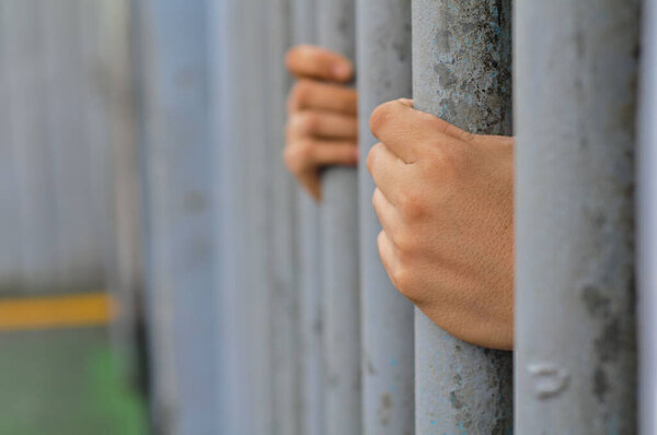 prisoner's hands behind bars with black background