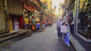 Dar bir sokakta motosikletli bir adam yürüyor.