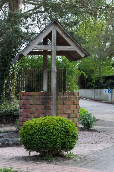 Üçgen ahşap çatılı eski bir kuyu. Ön planda yuvarlak bir çalı.