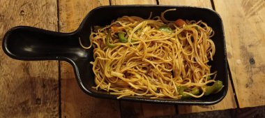 Dikdörtgen şeklinde siyah bir yemek, dilimlenmiş yeşil çan biberi ve muhtemelen havuçla karıştırılmış erişte (Chow Mein) pişirir..