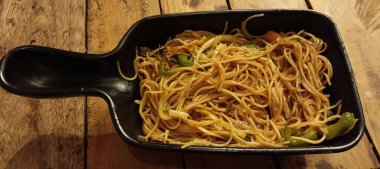 Dikdörtgen şeklinde siyah bir yemek, dilimlenmiş yeşil çan biberi ve muhtemelen havuçla karıştırılmış erişte (Chow Mein) pişirir..