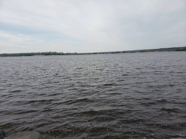 Mavi bulutlu gökyüzünün altında yeşilliklerle çevrili bir nehrin güzel görüntüsü.