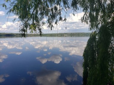 Nehir kıyısının güzel manzarası. Sularında yeşil ağaçlar var. Gökyüzü bulutlarla yansıtılıyor.