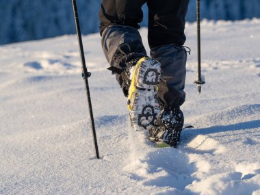 Close up of a man hiking on a mountain covered on snow, in boots with shoe skpikes. Outdoor winter trekking