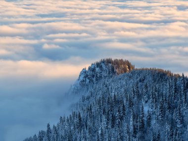 Aerial view of distant mountain peaks above clouds in clear sunny blue sky.