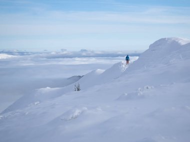 Man with backpack hiking on a mountain track above clouds in sunny day, Winter season with snow on mountain