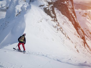 Lonely free-rider skier in high mountains. Extreme freestyle skiing in sunny daylight on winter mountain landscape