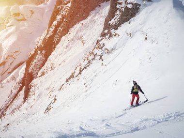 Lonely free-rider skier in high mountains. Extreme freestyle skiing in sunny daylight on winter mountain landscape
