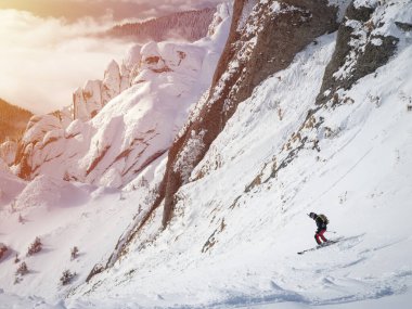 Lonely free-rider skier in high mountains. Extreme freestyle skiing in sunny daylight on winter mountain landscape