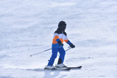 Speed and Adventure in the Sun: 10-Year-Old Boy Skiing Down a Sunny Slope with the Mountain in the Background