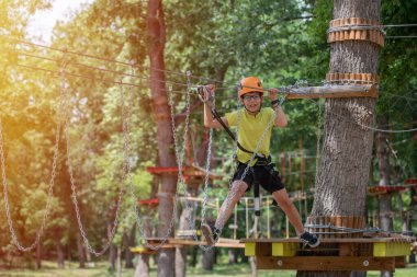 Oğlan ip kursuna tırmanmayı seviyor. Mutlu çocuklar macera parkında ip tutarak ve tahta merdivenlere tırmanarak oynuyorlar.
