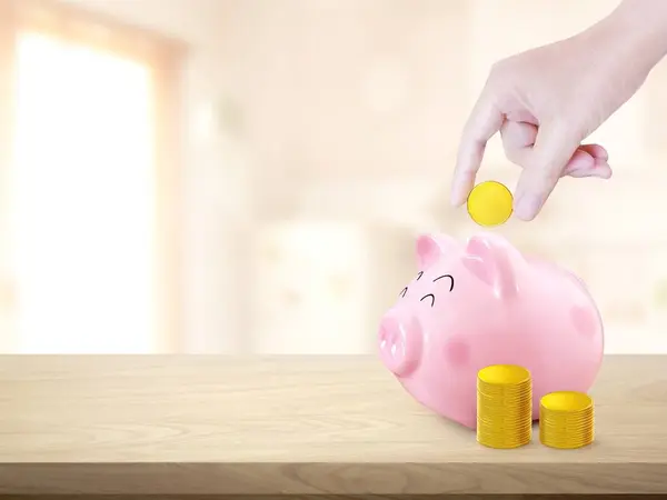Put the coins in the piggy bank with a pile of gold coins on the wooden table in the house.