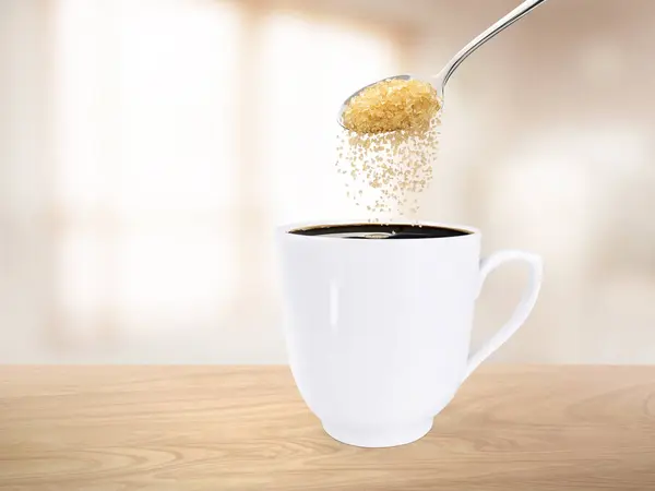 Spoon pour sugar into a coffee mug on the wooden floor inside the room.
