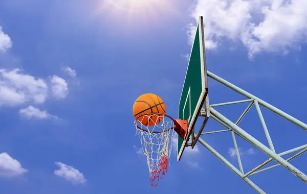 A basketball in a net on a blue sky background. The ball hit the ring. Sports, team game. Conceptual: victory, success, hitting the target, sport.