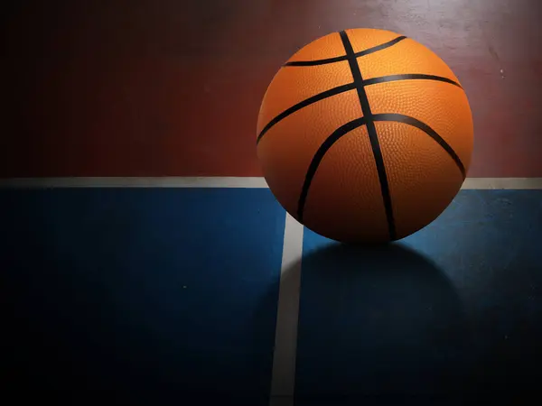 A basketball is placed on the red and green surface of the basketball court.