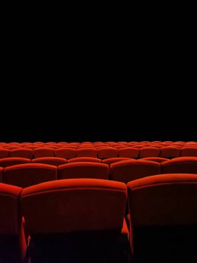 Kırmızı sandalyeler siyah arka plandaki boş bir sinemada düzgünce düzenlenir..