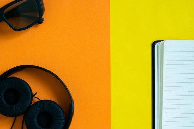 Kulaklık, güneş gözlüğü ve turuncu ve sarı arkaplan üzerine defter, düz görüntü