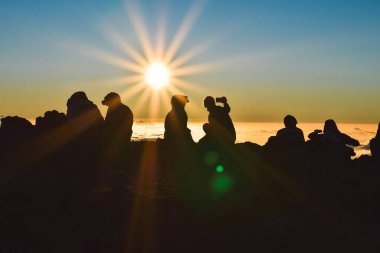 Bir grup insan dağdan gün batımını izliyor. Bir grup mutlu insan boş gün batımı plajında oturuyor..