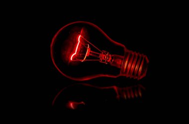 A light blub with red light in darkness. Old light bulb glowing with fossil fuel energy.  clipart
