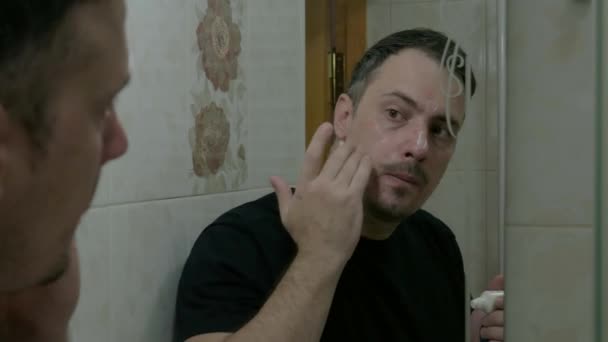 一个皮肤有问题的人在浴室里给自己的脸涂上治疗霜 一个在浴室里的年轻人在镜子前看着自己的时候照顾好自己的脸 — 图库视频影像