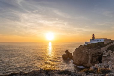 Farol do Cabo de Sao Vincente in Sagres in the Algarve Portugal. Overlooking the blue sea during a beautiful golden sunset clipart