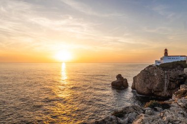 Farol do Cabo de Sao Vincente in Sagres in the Algarve Portugal. Overlooking the blue sea during a beautiful golden sunset clipart