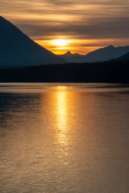 Arka planda gün batımı, karanlıkta bir dağ kenarı ve Alplerin eteklerinde bir göl.