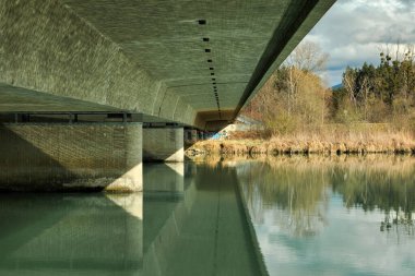 Baharda Bavyera 'da, Inn Nehri üzerindeki yol köprüsünün altından manzara. Yeşil su, gri beton.