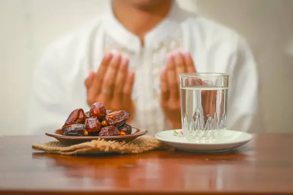 Allah 'a dua eden Müslüman elleri ile oruç yemeği ya da iftar yemeği. Masanın üzerinde bir bardak maden suyu olan tarihler.