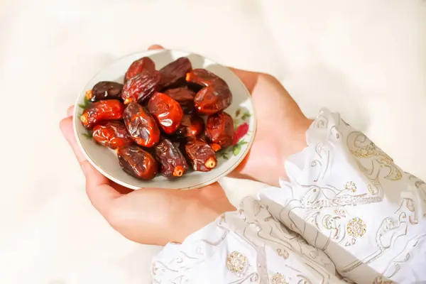 Ramazan Kareem kavramı. Müslüman bir kadının ellerinin tatlı hurmalarla dolu bir tabağı paylaşması. Cömertlik ve Ramazan geleneklerinin sembolü.