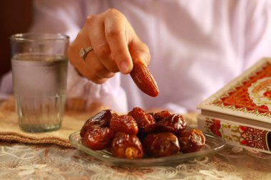 Allah 'a dua eden Müslüman kadınların elleriyle oruç yemeği ya da iftar tabağı. Masanın üzerinde bir bardak maden suyu olan tarihler. Geleneksel Ramazan, fast-break yemeği. Endonezya - 13 Mart 2024