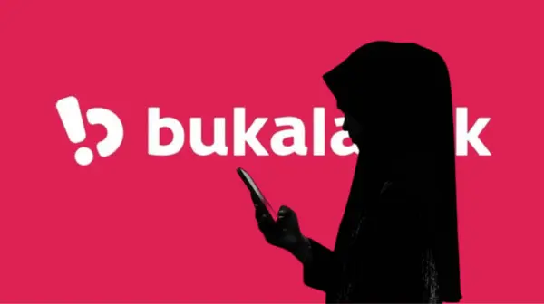 Endonezya-13 Mart 2024: Bukalapak logosu olan büyük ekranın önünde akıllı telefon tutan bir kadın