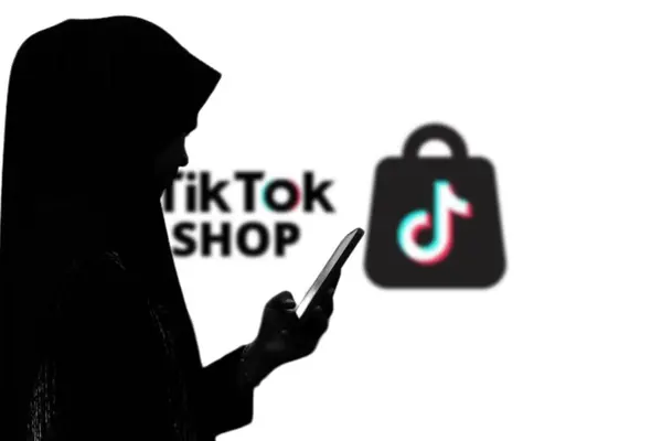 Arka planda TikTokshop logosu olan büyük bir ekranın önünde akıllı telefon tutan bir kadın. Endonezya - 13 Mart 2024.