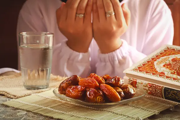 stock image Fast breaking meal or iftar dish with muslim woman hands praying to Allah. Dates with a glass of mineral water on the table.Traditional Ramadan, fast breaking meal. Indonesia-March 13,2024