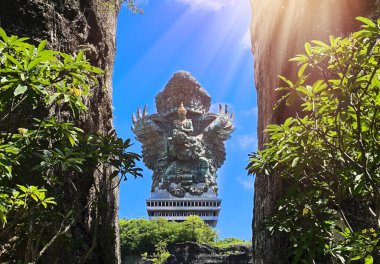 Garuda Wisnu Kencana heykelinin iki kaya duvarı arasındaki portresi, Bali 'de ikonik bir kültür simgesi, arka planda mavi gökyüzü olan GWK Kültür Parkında.