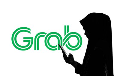 Indonesia - April 4,2024: Woman is holding a smartphone in front of a large screen with Grab company logo clipart