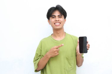 Yeşil tişörtlü gülümseyen genç adam elinde akıllı telefon, beyaz bir arka planın karşısında duruyor.