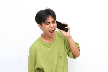 Yeşil gömlekli genç adam gülümsüyor ve akıllı telefonuyla neşeli bir ifadeyle konuşuyor, beyaz bir arka plana karşı duruyor.