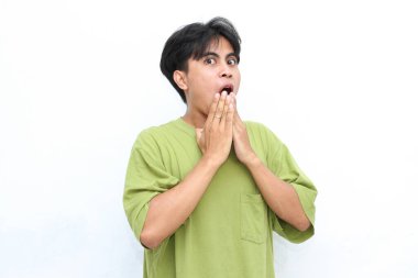 Yeşil gömlekli genç adam beyaz arka planda iki eliyle ağzını kapatıyor. Komik, şok olmuş yüz ifadelerini vurgulamak