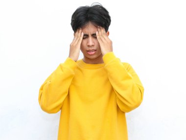 Sarı kazaklı genç adam beyaz bir arka planda acı dolu bir ifadeyle iki eliyle başını bastırıyor.