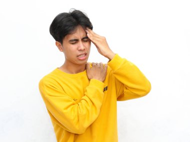 Sarı kazaklı genç adam beyaz bir arka planda acı dolu bir ifadeyle iki eliyle başını bastırıyor.