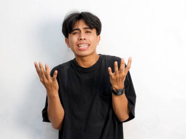 Siyah tişört giyen Asyalı genç bir adamın beyaz arka planda izole edilmiş bir şeye tepki göstermesinin komik bir portresi.